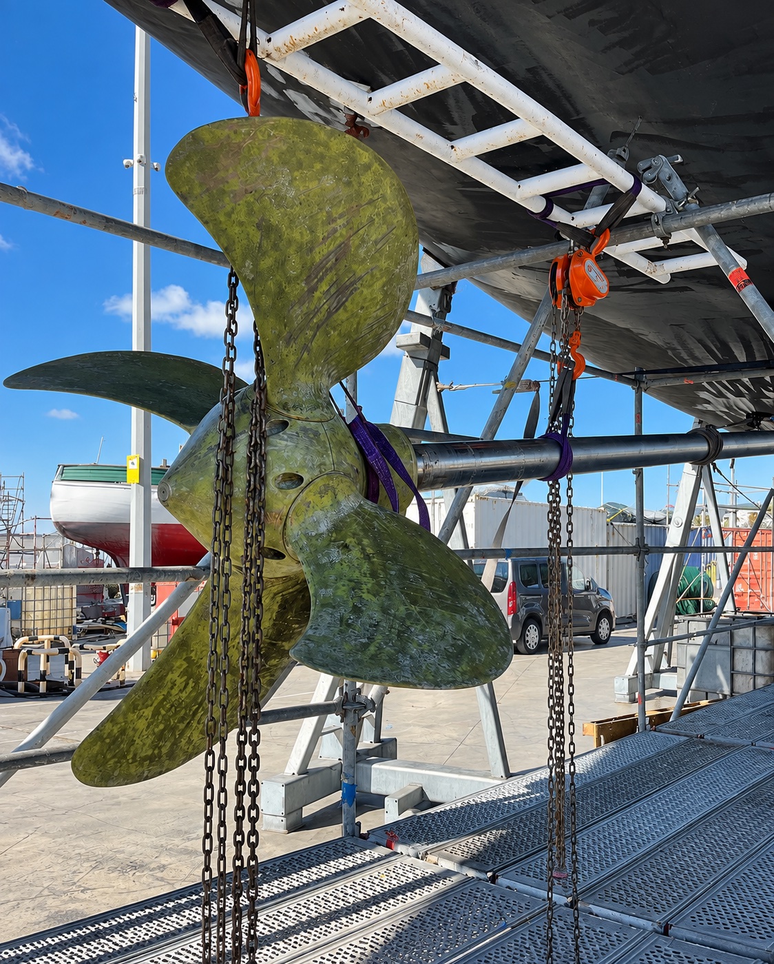 Propeller hanging from chains beneath a hull in the boatyard