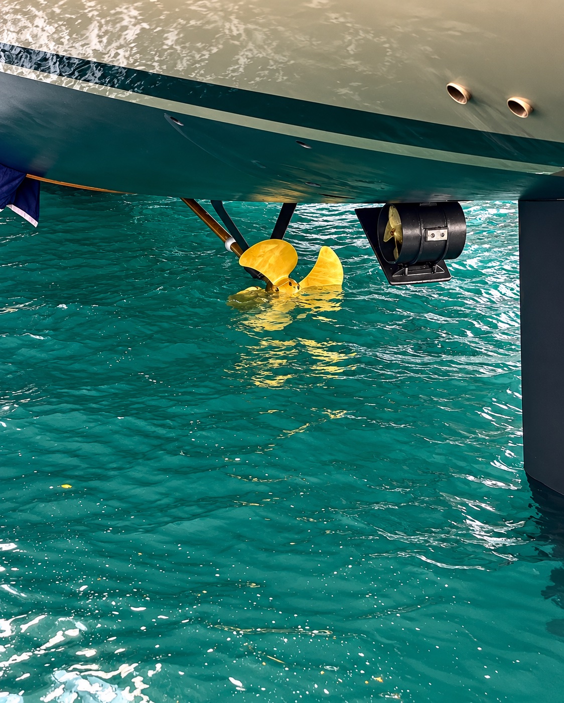 Yellow propeller and thruster beneath a hull in clear turquoise water
